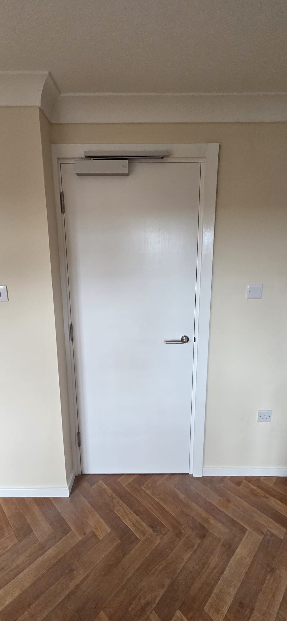 Certified white FD30 fire door with overhead door closer installed in a residential communal corridor