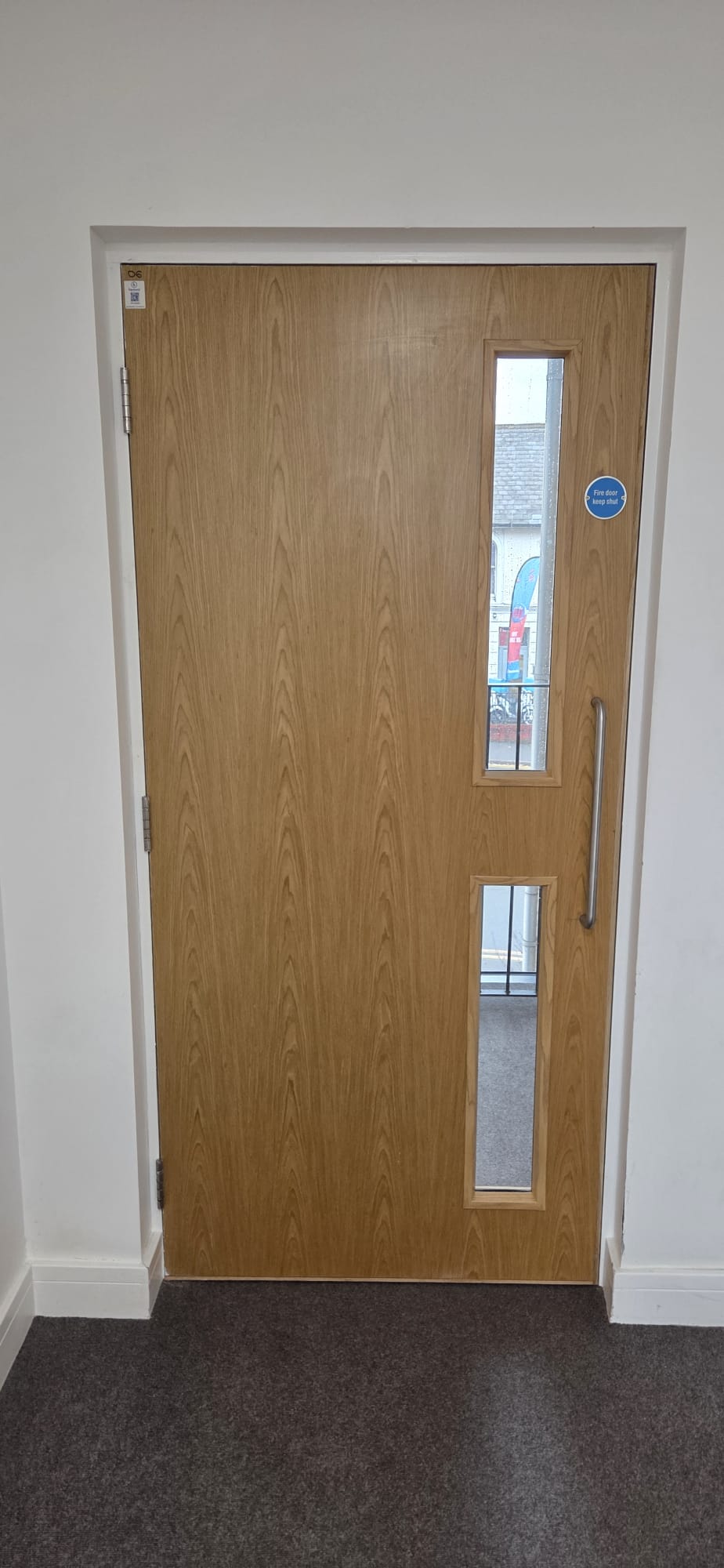 Certified oak veneer fire door with twin vision panels and BM TRADA data plug installed in a commercial entrance