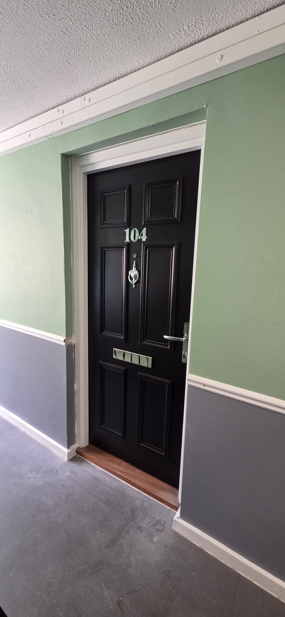 Certified black composite flat entrance fire door with letter plate installed in a housing block corridor