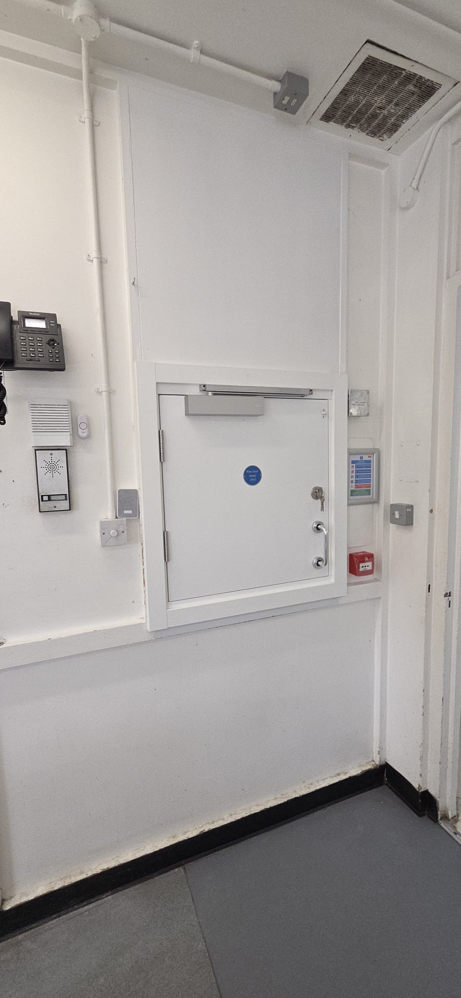 Certified white fire-rated riser access door with door closer installed in a service cupboard