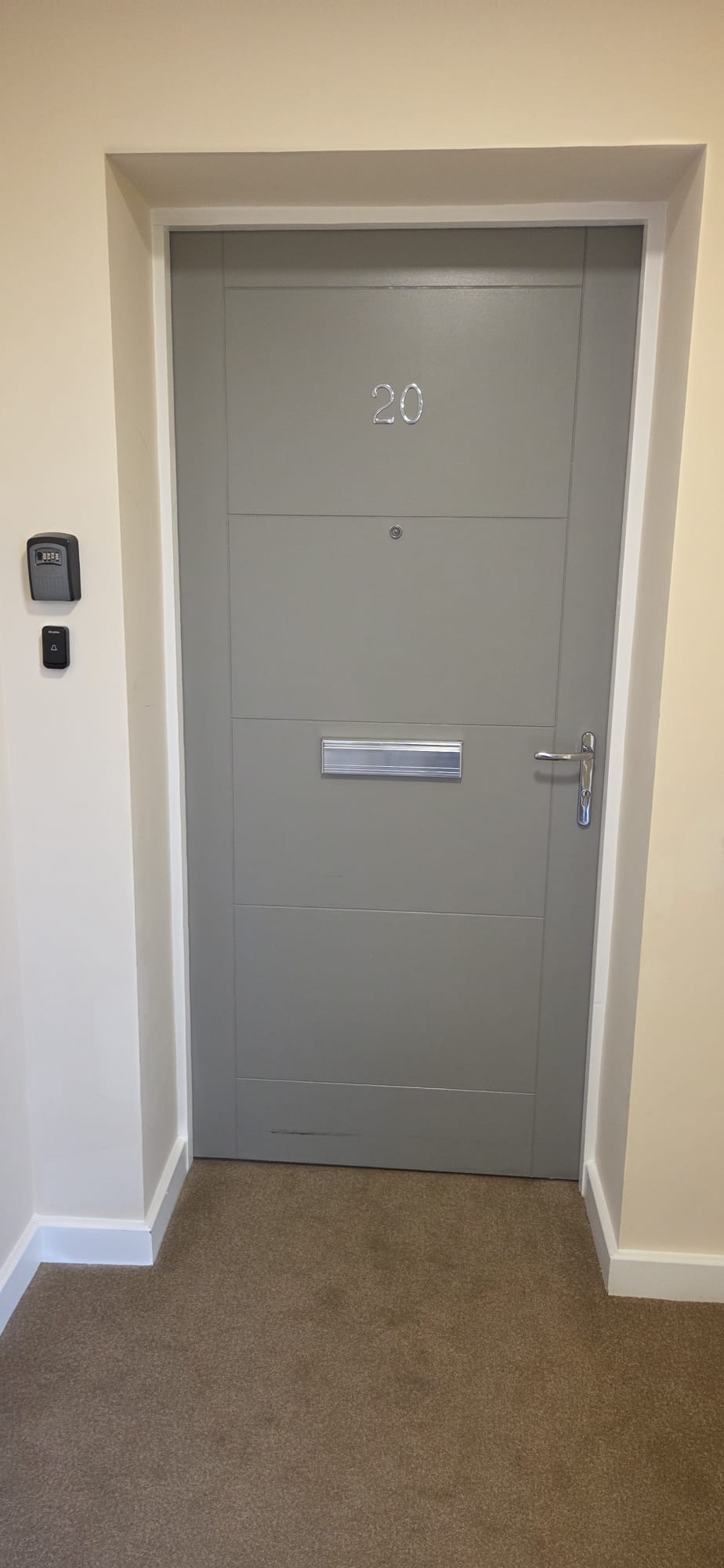 Certified grey composite flat entrance fire door with chrome letter plate installed in a residential corridor