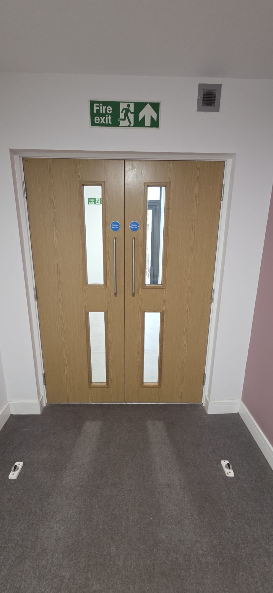 Certified oak veneer double fire doors installed on a protected escape route beneath a fire exit sign