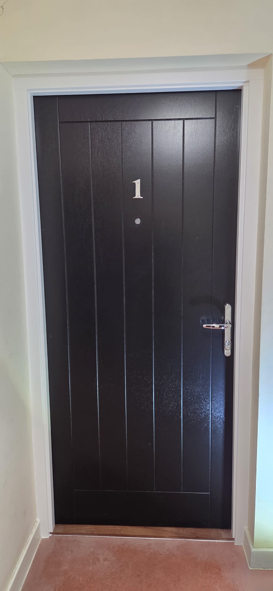 Certified black planked composite flat entrance fire door installed in a residential lobby