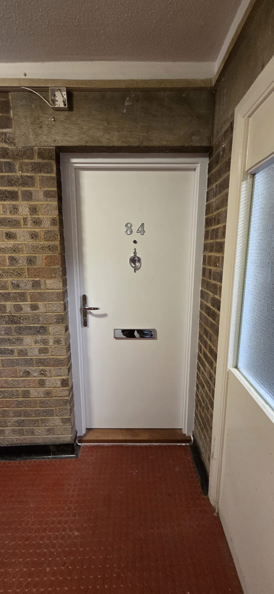 Certified white flat entrance fire door installed in a communal walkway with brick surround