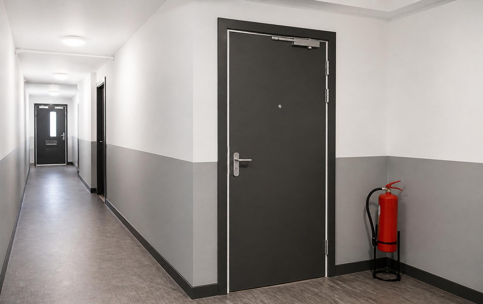 Communal corridor after FRA passive fire remedial works — new fire door, fresh compartment walls, extinguisher
